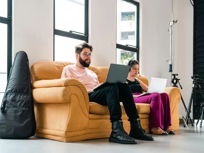 Two freelancers sitting on a couch with laptops in a bright studio space, focusing on their projects for Town Network Directory